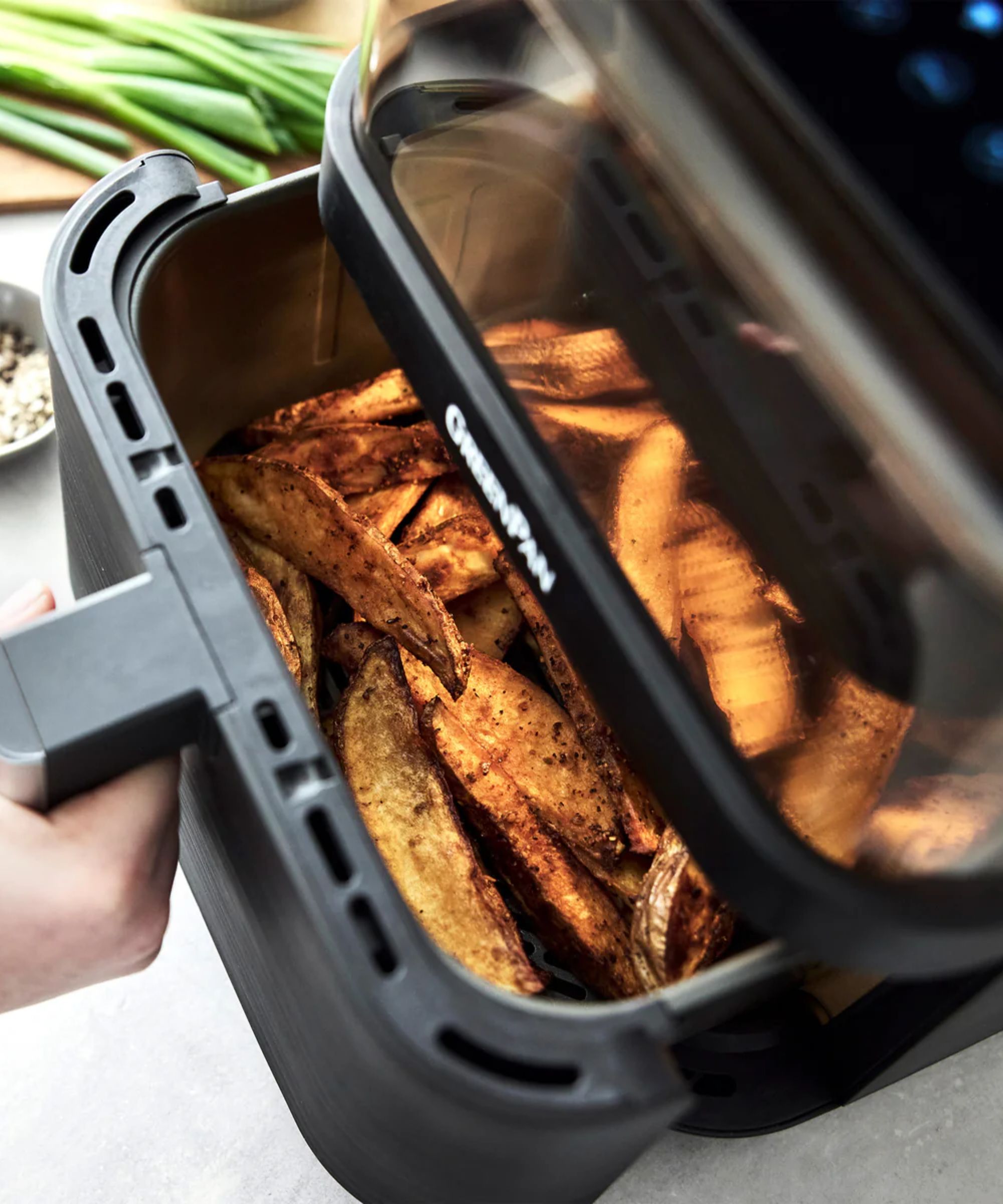 The GreenPan Bistro 360 Clear View Air Fryer is being partially opened to show crisp home fries.