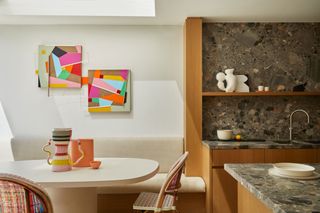 a luxury kitchen extension with brown natural stone surfaces. a skylight sits above a dining area with colorful artwork and vases