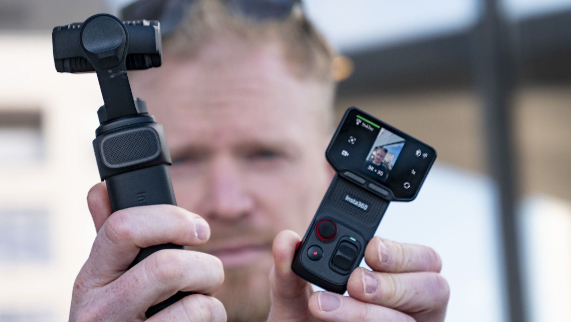 Man holding the Insta360 Luna Ultra vlogging camera and its screen, outdoors in a grey urban scene