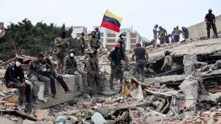 Rescuers search for victims at a collapsed building as one raises a Venezuelan flag following a magnitude earthquake that struck Venezuela on June 28, 2026