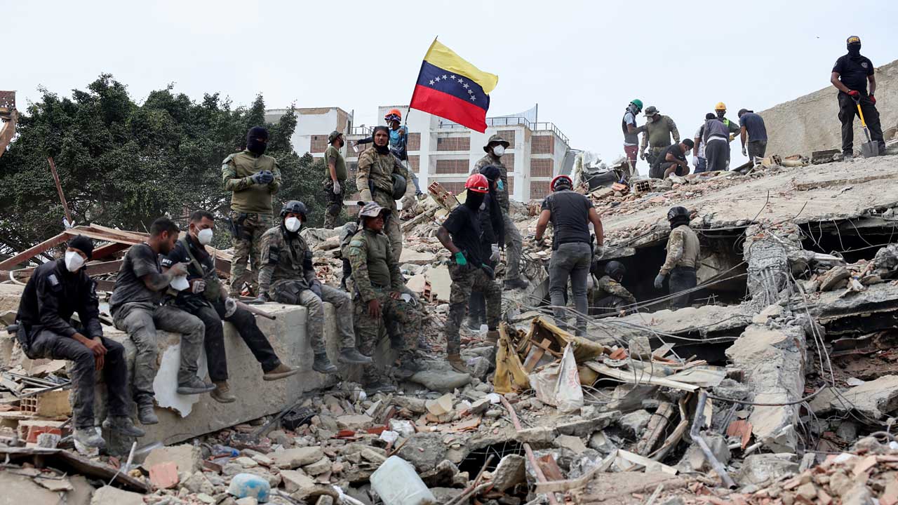 Rescuers search for victims at a collapsed building as one raises a Venezuelan flag following a magnitude earthquake that struck Venezuela on June 28, 2026
