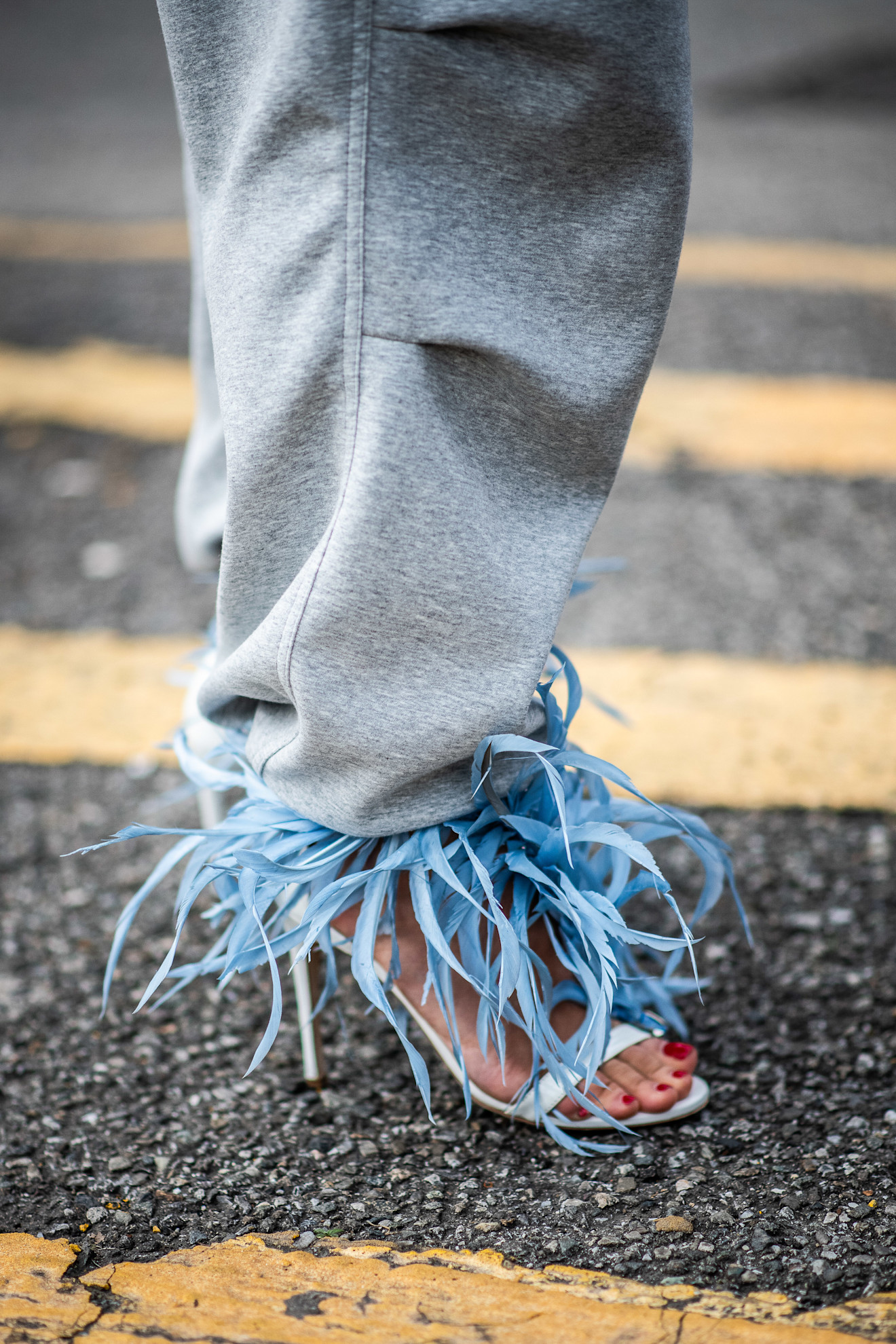 a close up of a blue feathered shoe with gray pants and red toenails