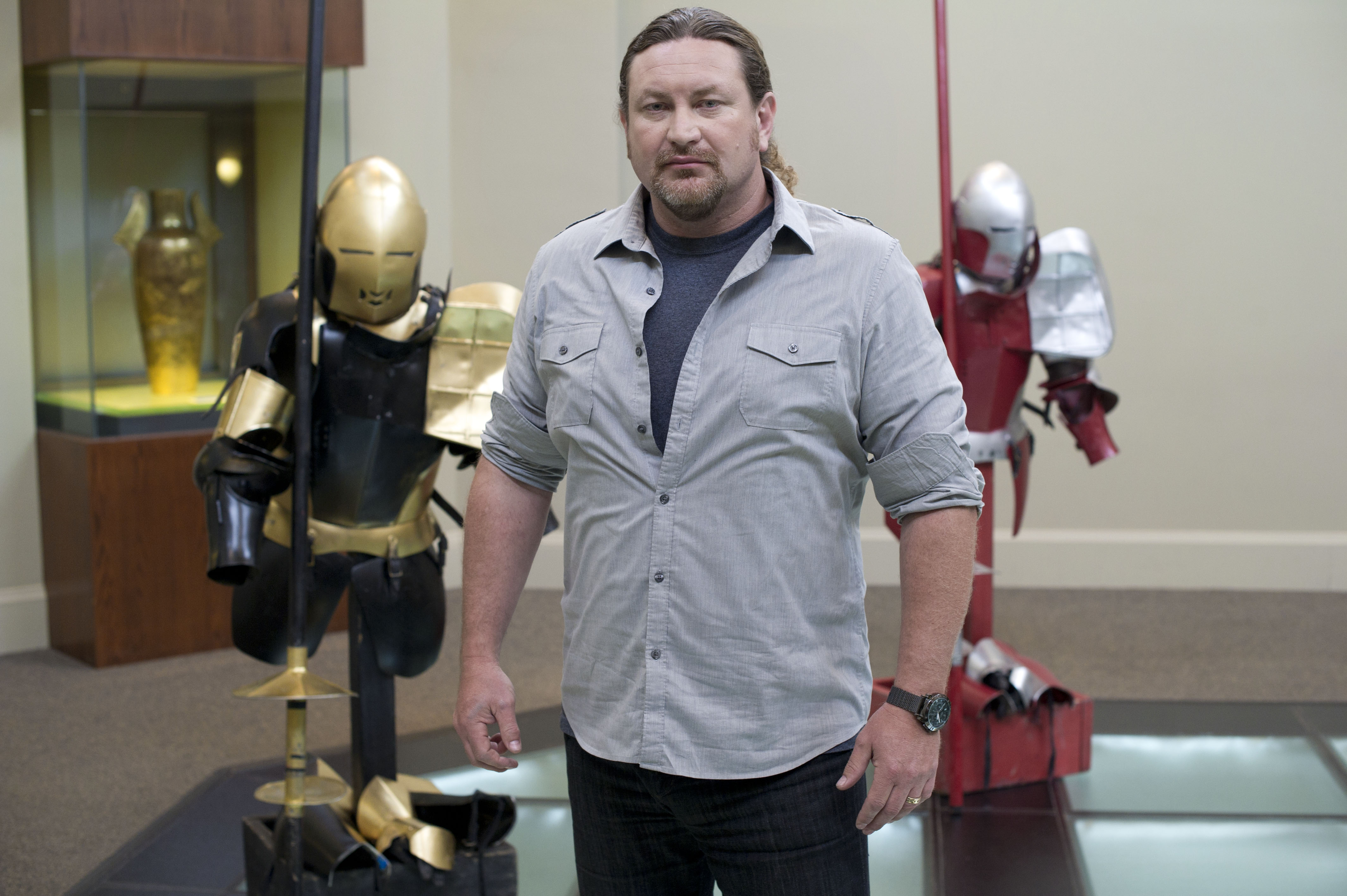 a man stands in front of two josting uniforms in the tv show 'Full Metal Jousting'