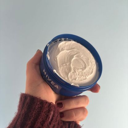 a hand holding an open tub of nivea creme