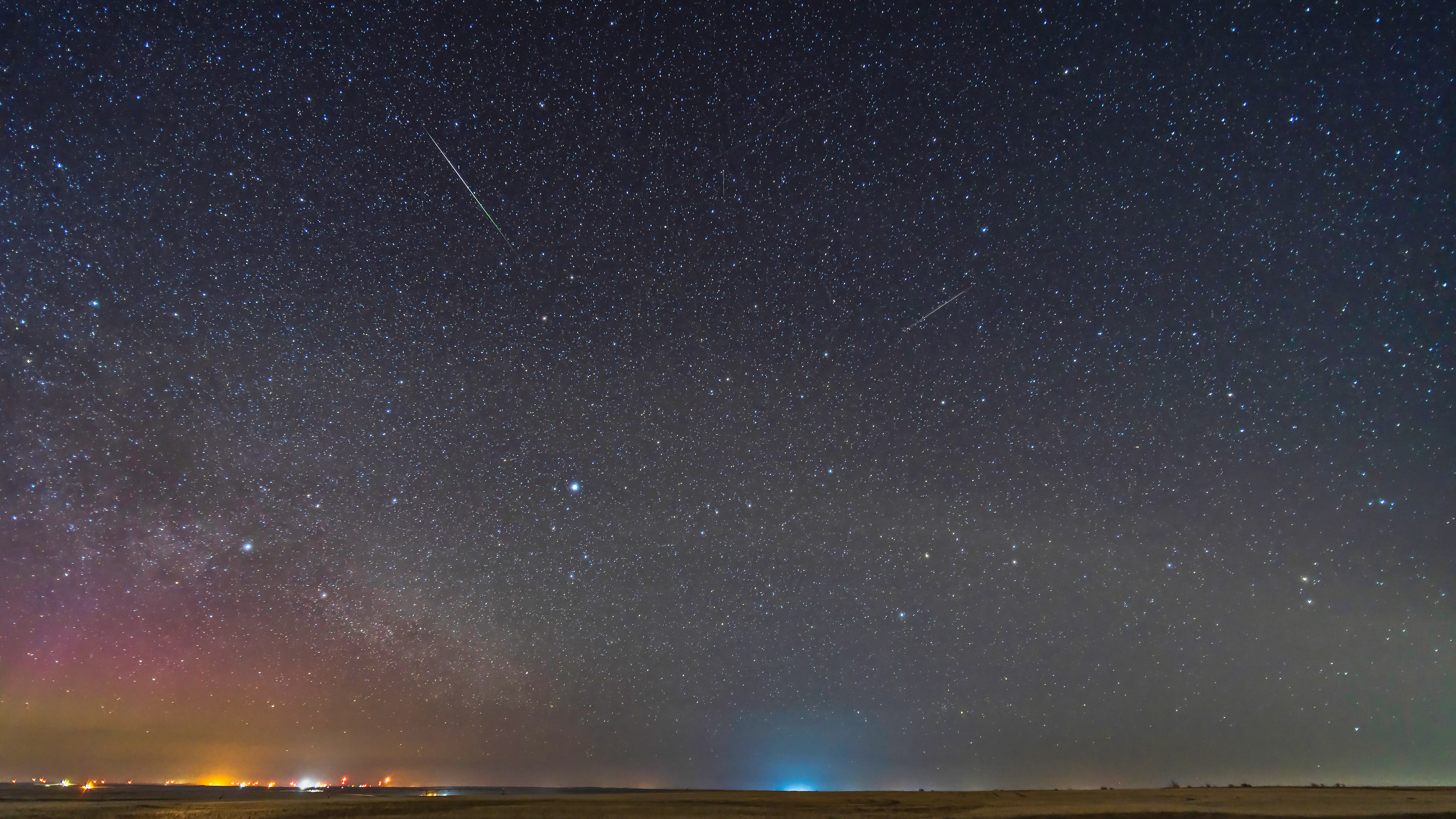 Two lone Lyrid meteors on the peak of the meteor shower night, April 22, 2023. The sky and ground come from the exposure with the bright meteor on it, when a dim aurora was also on the northeast horizon. The bright meteor shows the classic green to pink gradient of colours. Vega and Lyra are rising at lower centre. Deneb and Cygnus are at left. Arcturus is at upper right
