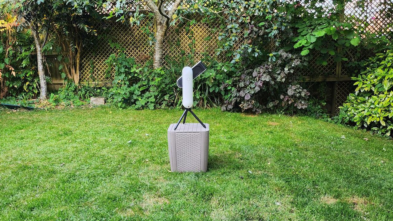 The Vaonis Vespera Pro pointed upwards with the power button visible with trees and grass in the background.