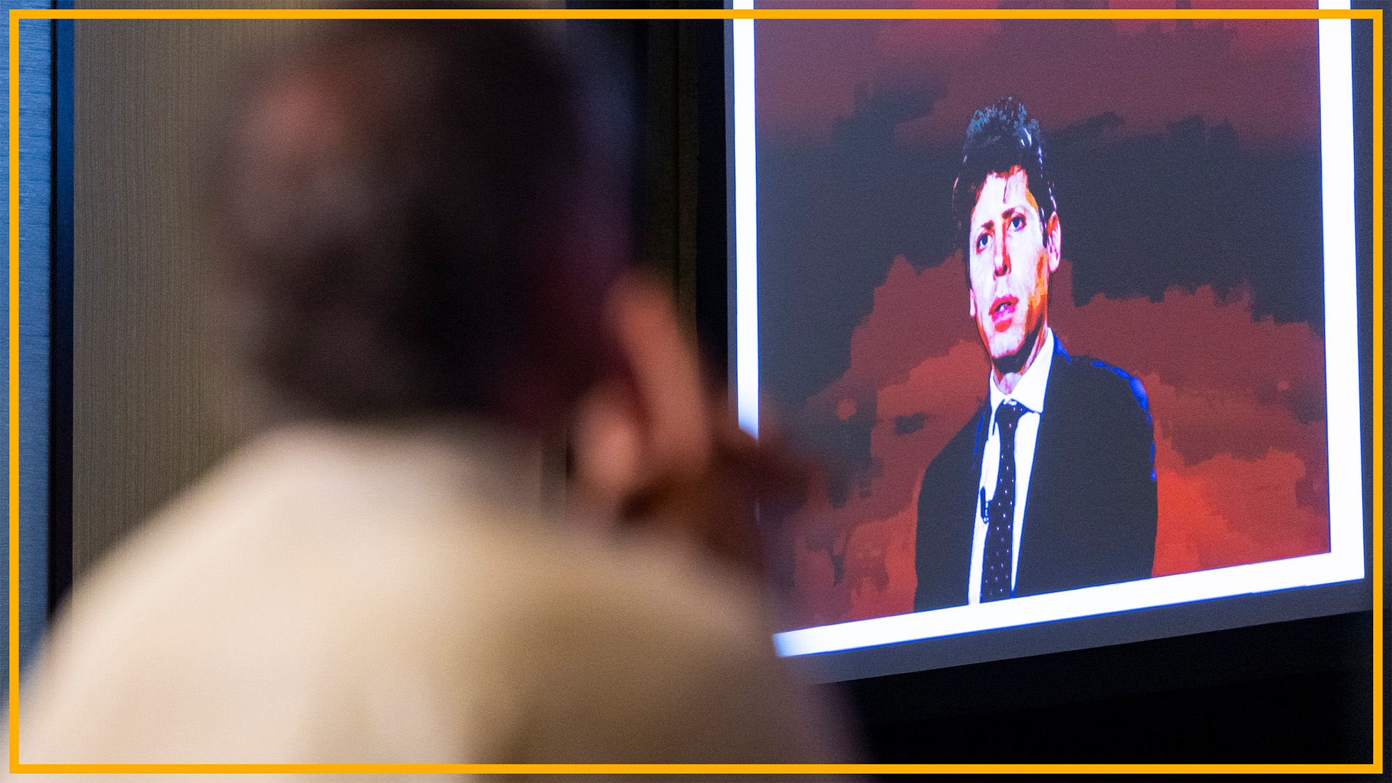 A man looks at a presentation with a man in front of a red background