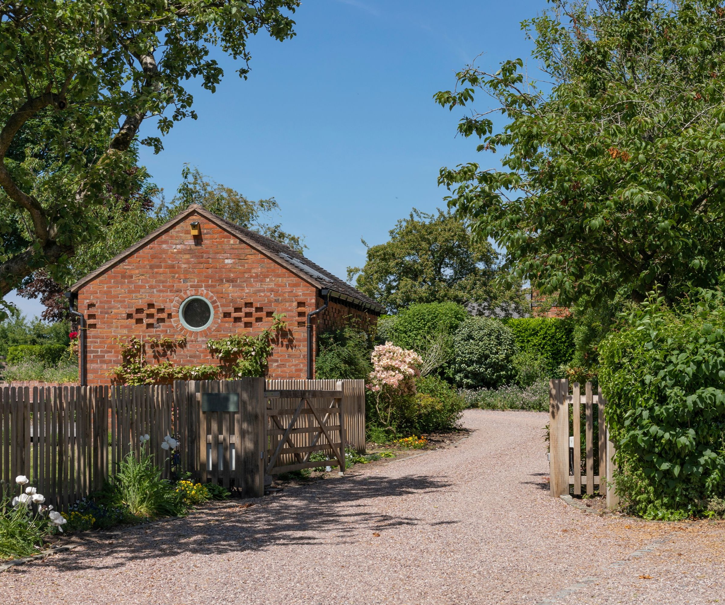 gravel driveway with wooden fencing and a small redbrick outbuilding