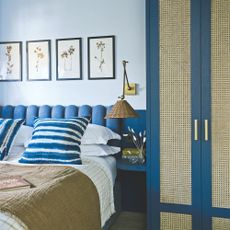 light blue painted bedroom with dark blue scalloped headboard and matching wardrobe with rattan inserts