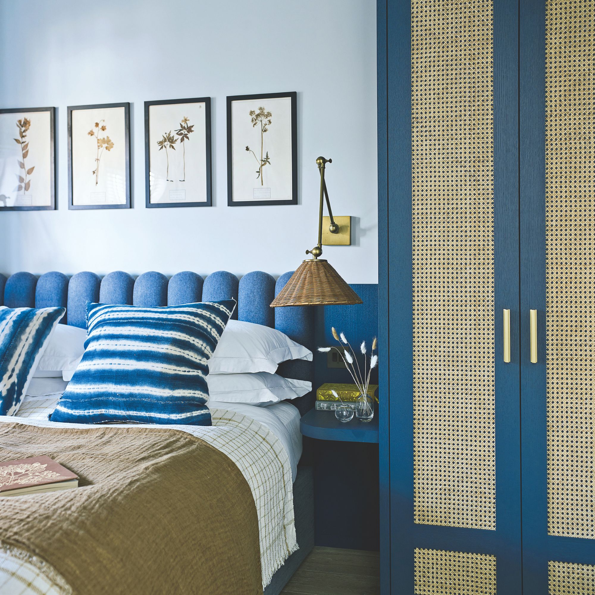 light blue painted bedroom with dark blue scalloped headboard and matching wardrobe with rattan inserts