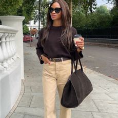 Woman wears brown jumper, beige trousers and brown bag