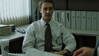 Edward Norton in a shirt and tie with a starbucks cup on his desk in Fight Club