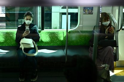 Women look at their phones on the train in Tokyo.