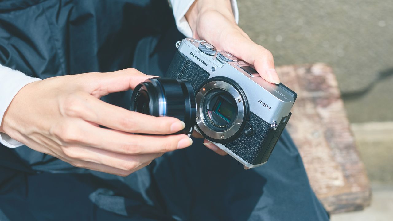 Person putting a lens on the OM System PEN camera
