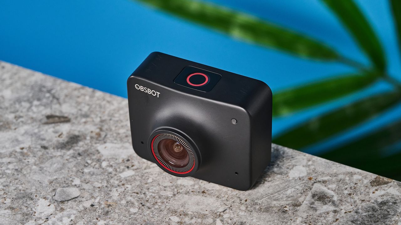 a black small 4K webcam with a red button photographed on a beige surface against a blue background
