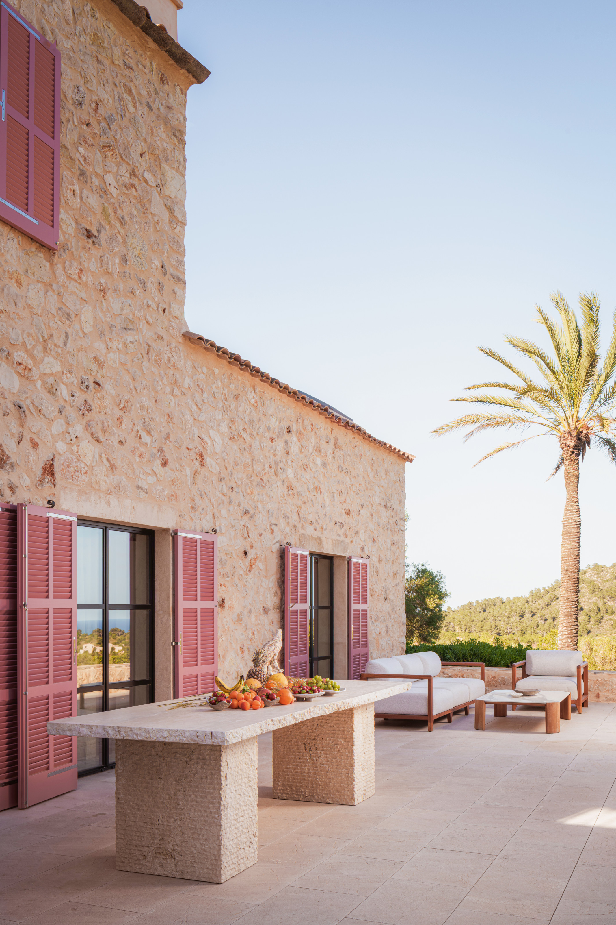 Outdoor area with stone table, pink shutters and white and wood seating