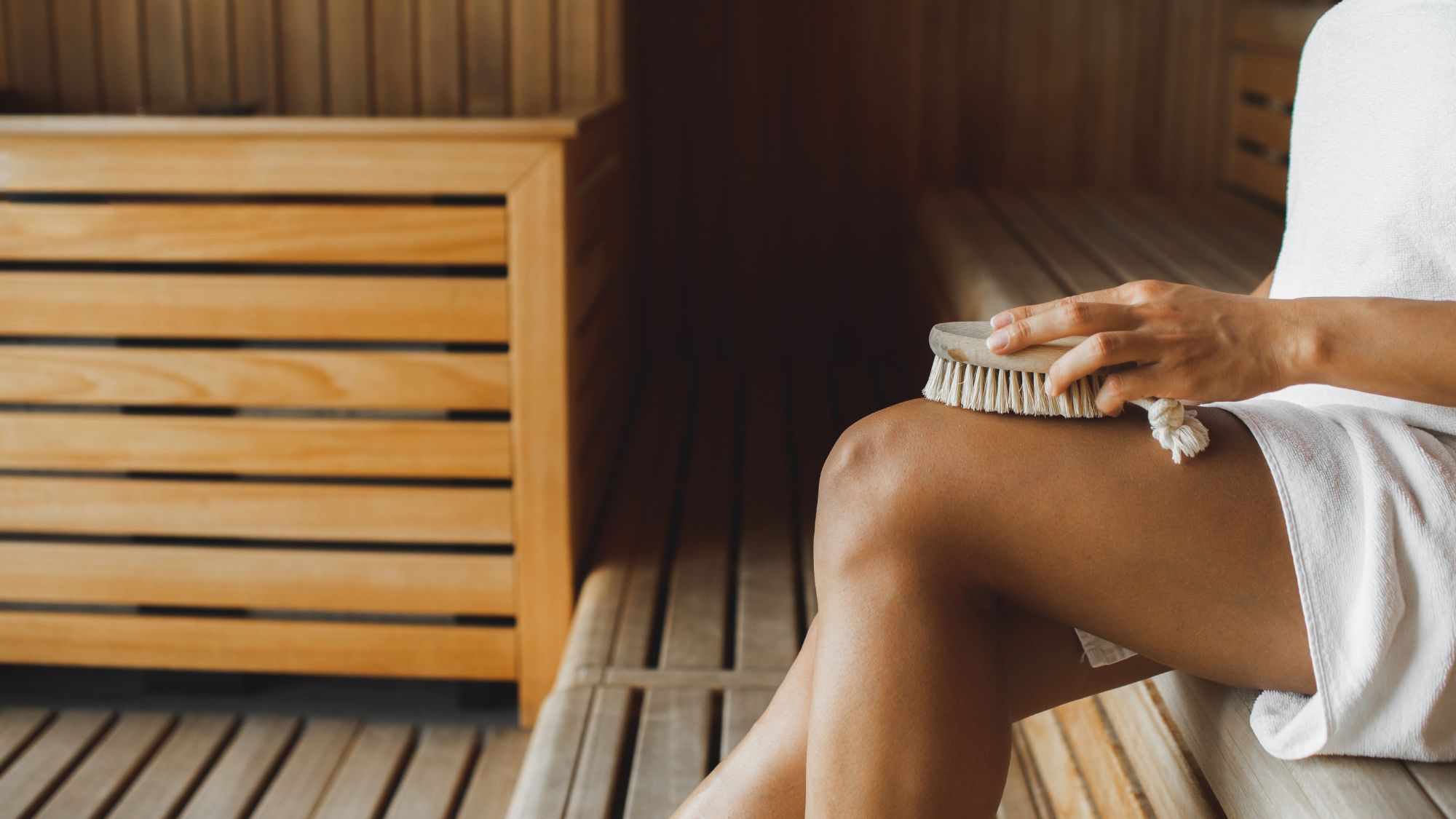 woman dry brushing her legs in a sauna
