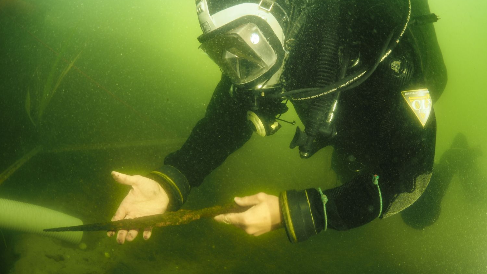 A diver holding a medieval spearhead under the murky waters of Lake Lednica in Poland.