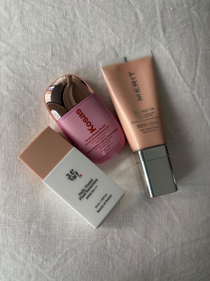 Three tinted SPFs on a white linen background