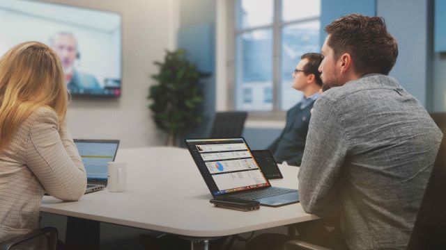 Office workers sitting at a desk with Jetbuilt and Kinly technology. 