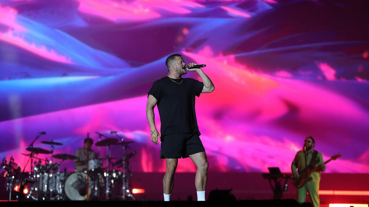 a rock band plays on a large stage in front of a colorful psychedelic backdrop