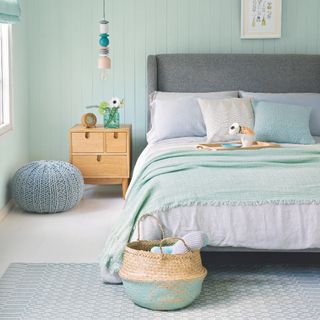 coastal bedroom ideas with aqua green walls and throw, baskets, knitted footstool, grey bed, blond wood bedside, white floorboards, tray, pendant lamp, artwork
