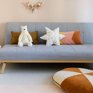 A living room witha grey sofa bed with a star-shaped and patchwork cushions and a stuffed toy