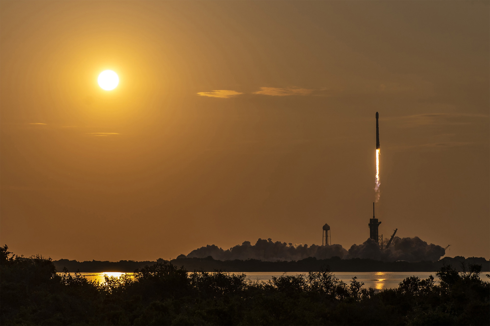 A photo of SpaceX's Falcon 9 rocket launches with the rising sun.