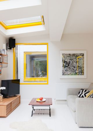 an open-plan kitchen with yellow framing on the windows. In the living room there is also a sofa and a tv opposite it. In the middle of the room is a coffee table