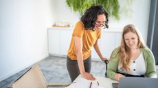 Two women collaborate using a laptop in a modern office