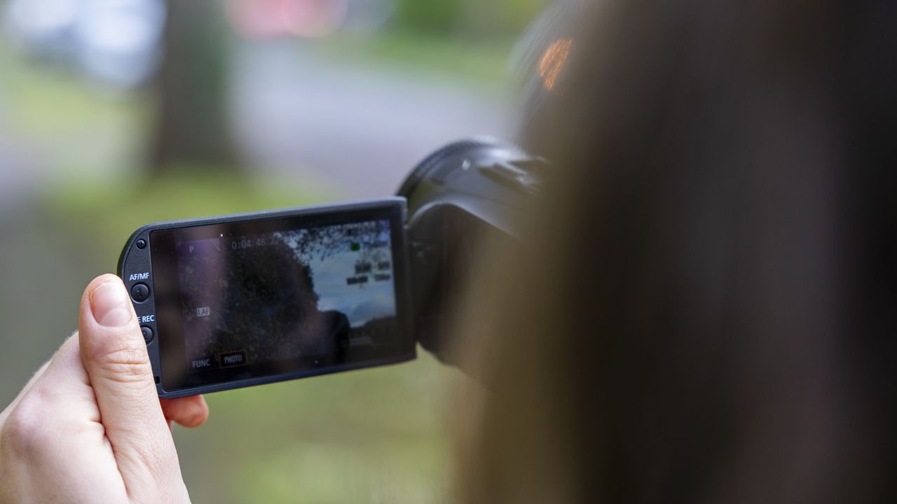 A woman holding the Canon HF G70 on a suburban street