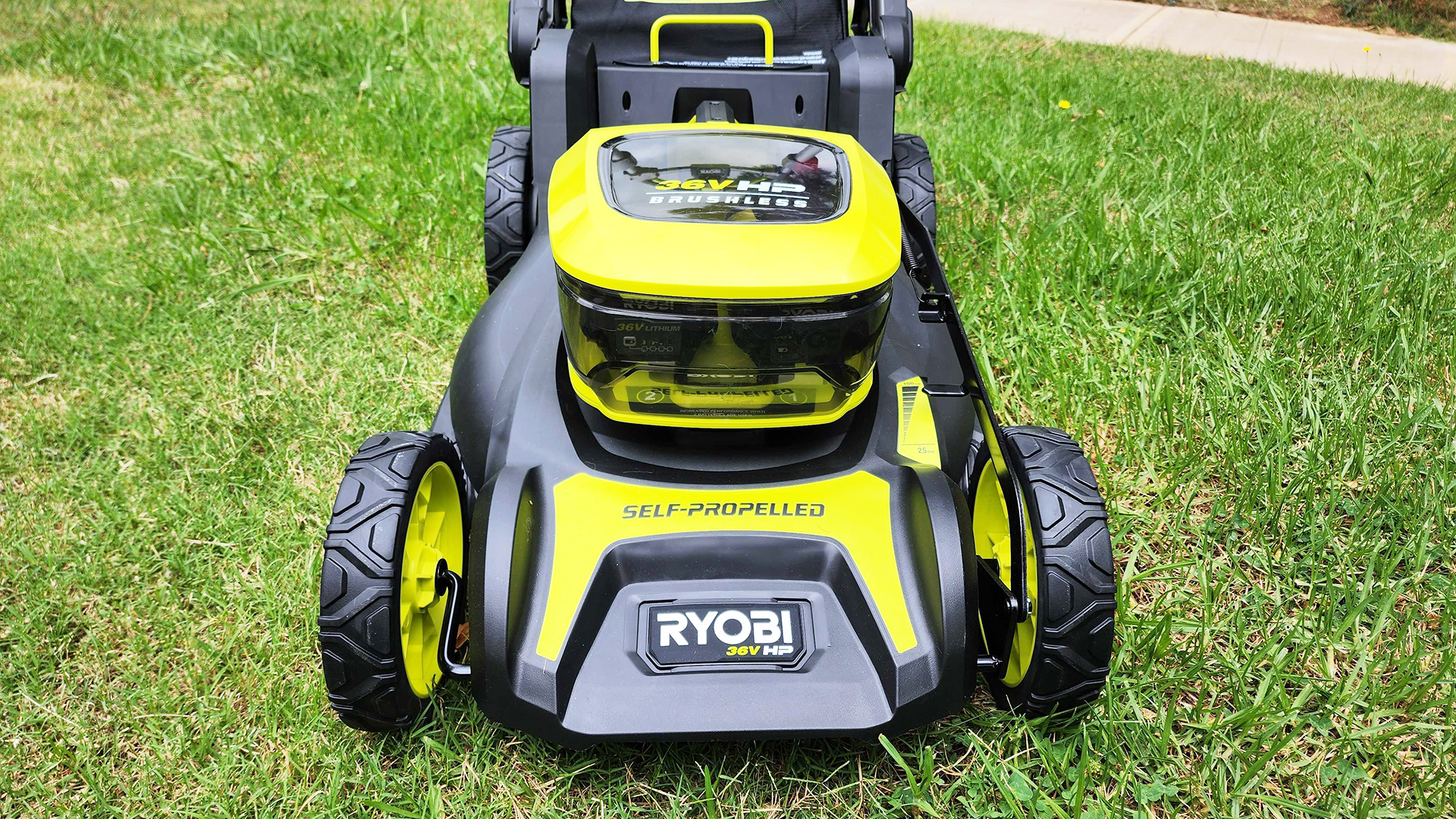 Ryobi 36V HP 46cm 6.0Ah Brushless Cordless Lawn Mower on a lawn with street in the background