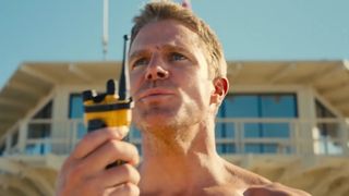 Stephen Amell as Hobie Buchanon in Baywatch. Hobie is using a yellow walkie talkie and signaling for help after a plane crashed into the ocean.