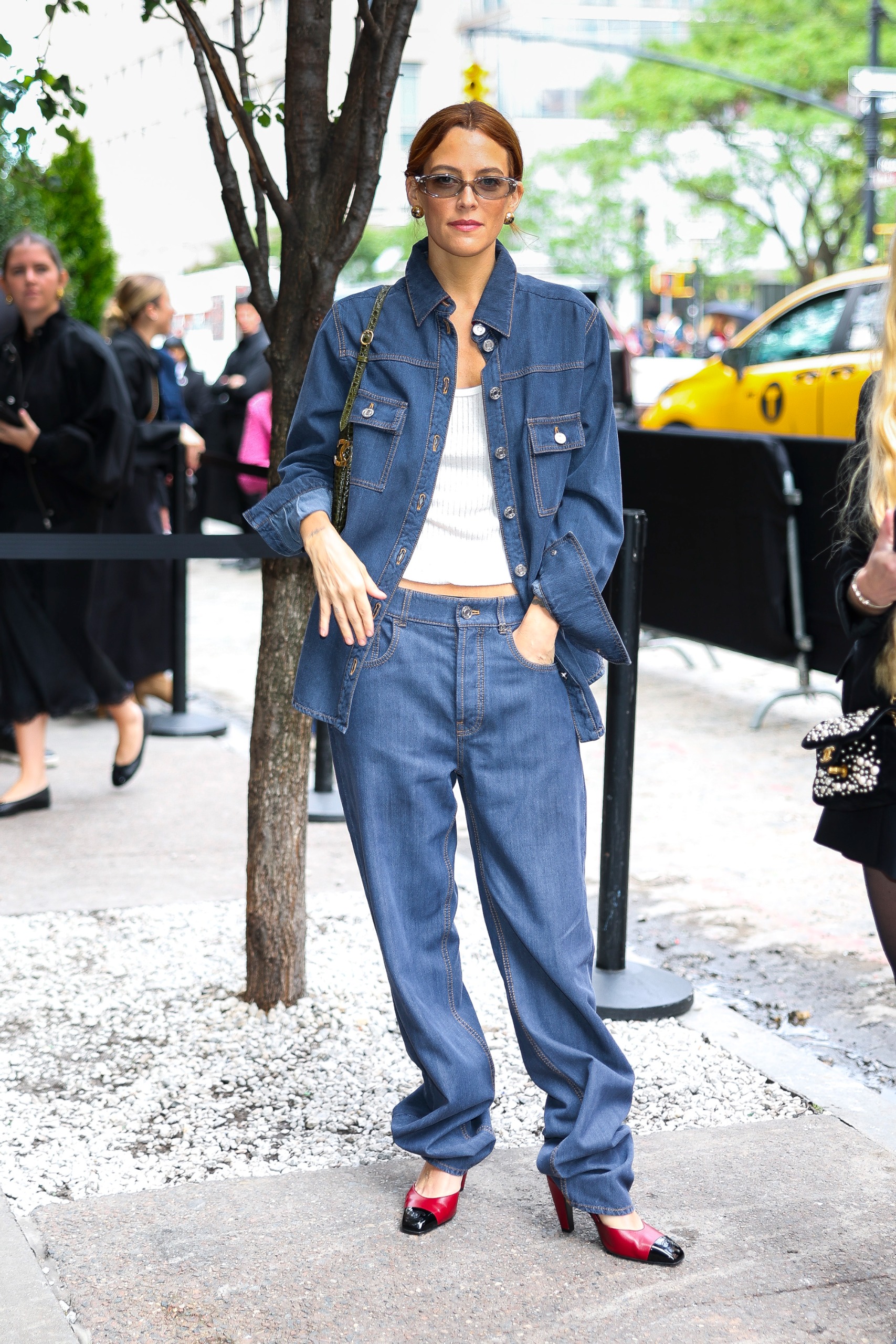 Riley Keough wears low-rise puddle jeans with red and black Chanel heels and a denim jacket at a Chanel event in New York.