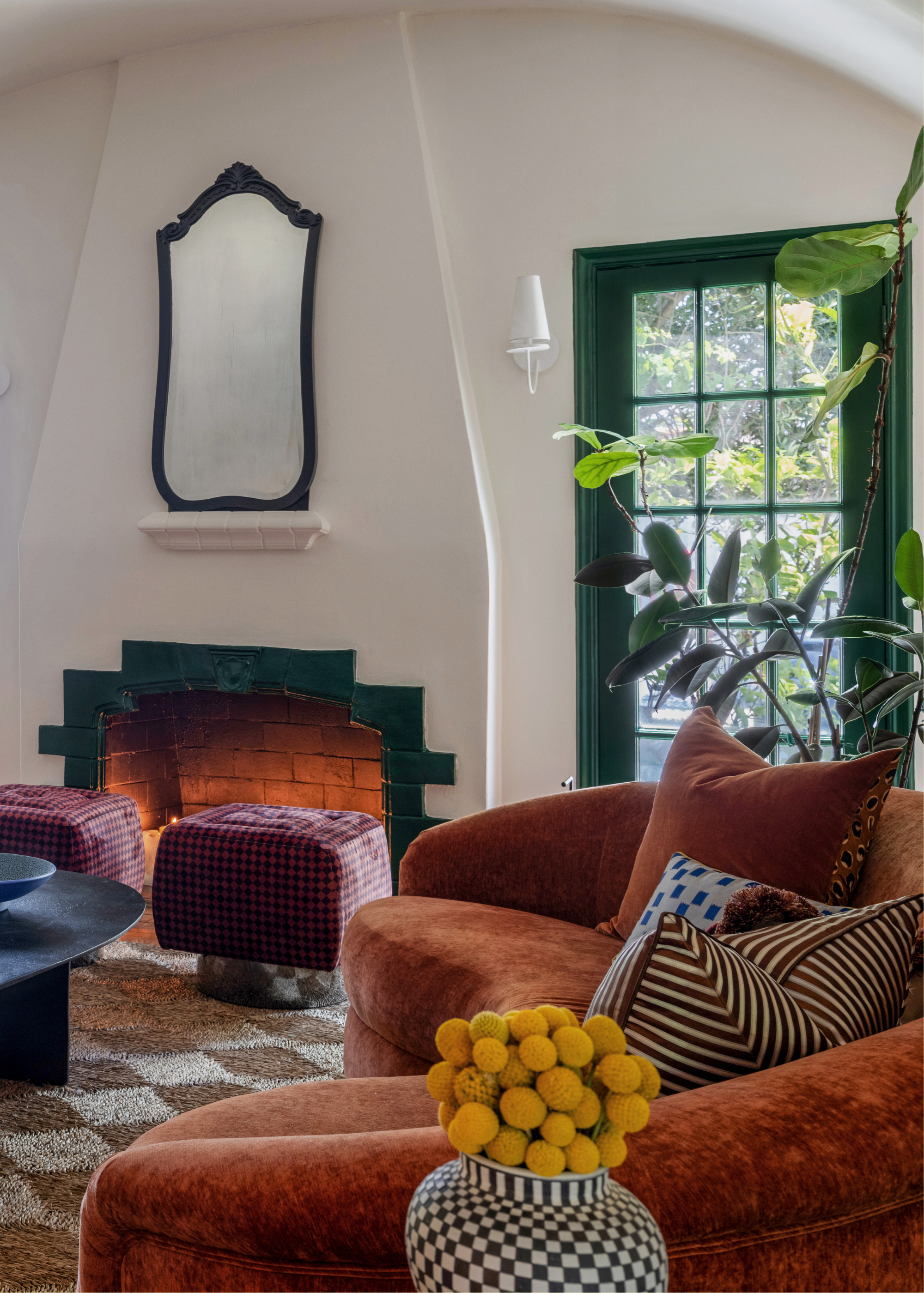 A living room with a vase of marigolds by a burnt orange couch with patterned pillows