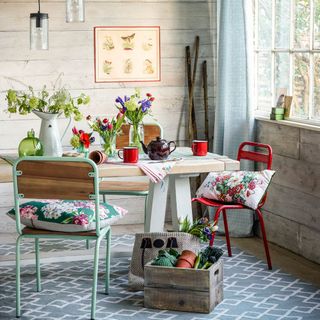 A country dining room with wood panel-effect wallpaper, pendant lights and flowers on a table