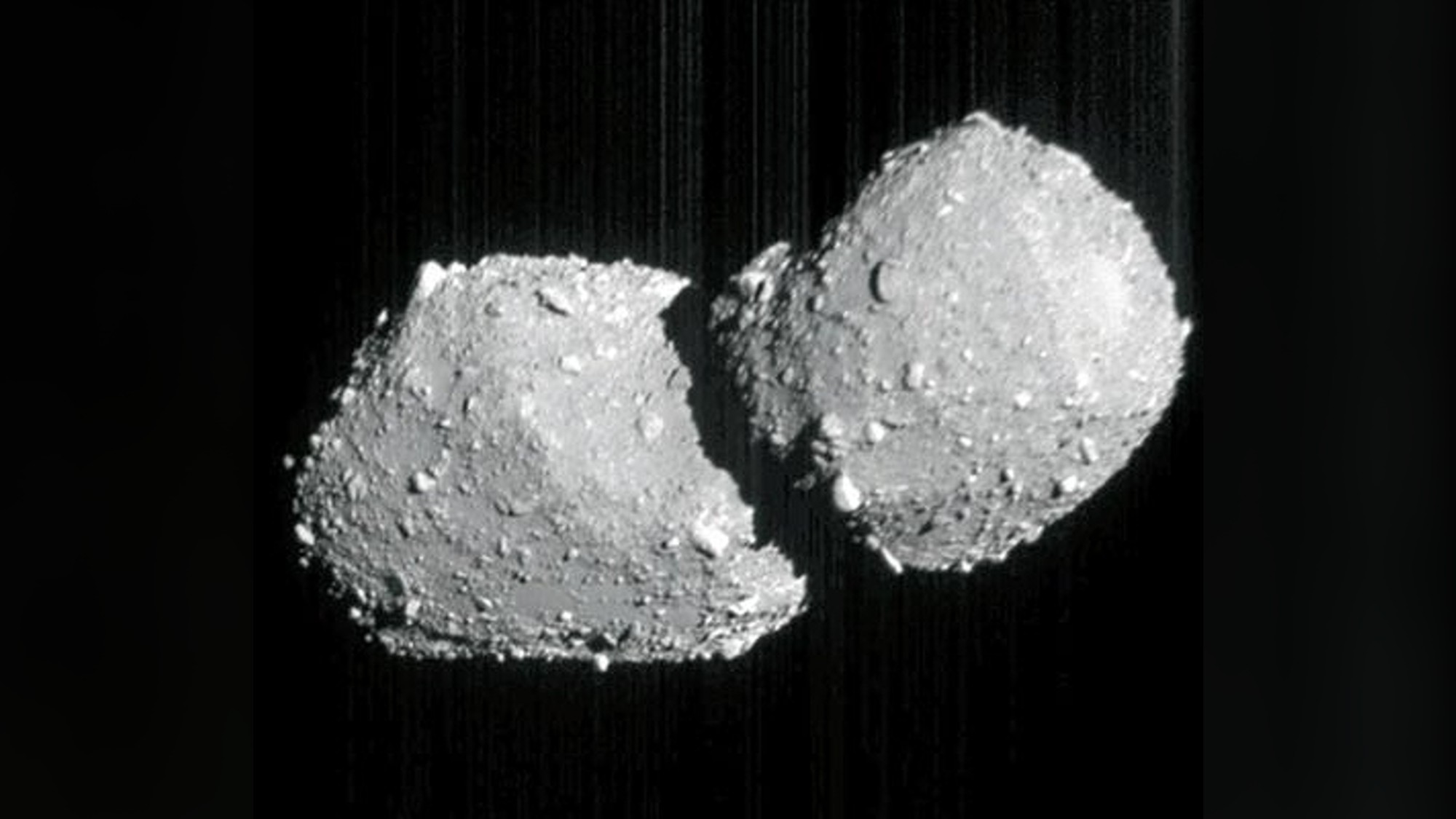 a grey, double-lobed rock on a black background. the surfaces of the two lobes are covered in boulders of various sizes