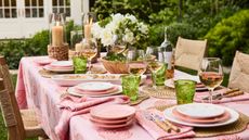 Outdoor table set up with pink tablecloth, green glasses, rattan accessories