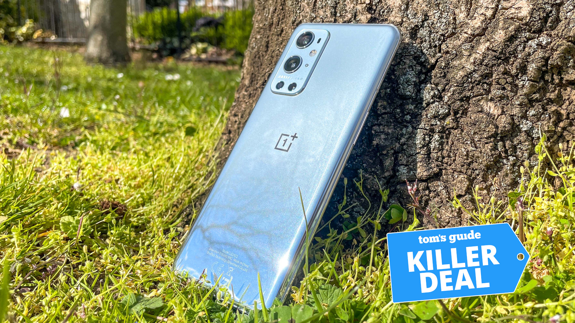 oneplus 9 pro leaning against a tree in the grass with killer deal tag