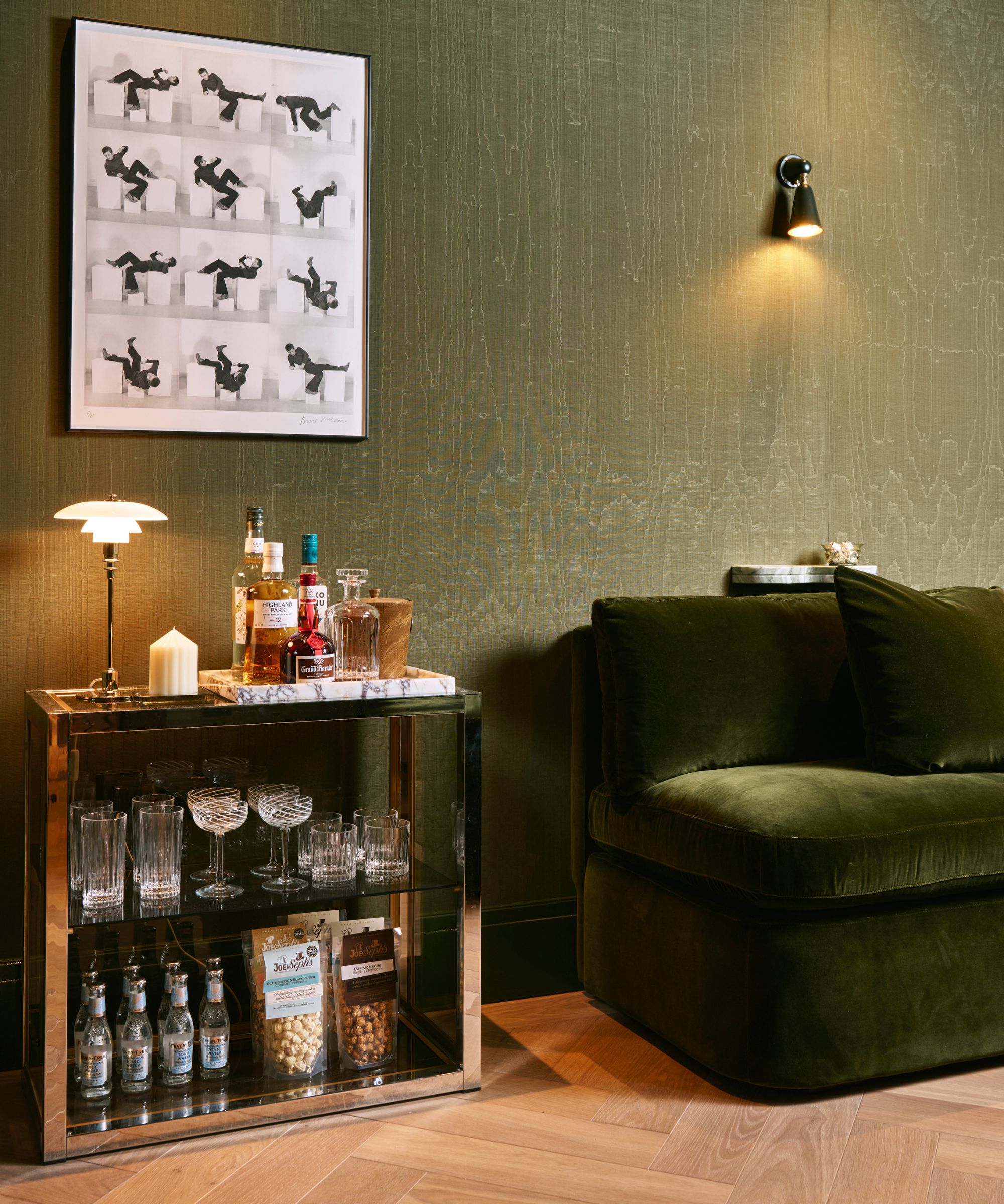 a green wallpapered cinema room with a dark green velet couch and mini home bar