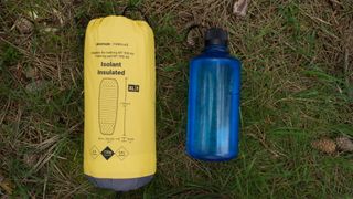 A packed Forclaz Inflatable Trekking Mattress MT900 on some grass next to a large water bottle.