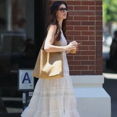 Camila Morrone wears a white sundress, coach brooklyn bag, and cowboy boots.