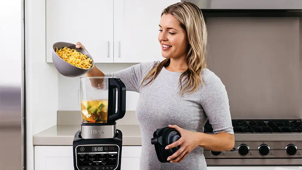 A woman adding fruit to a Ninja blender