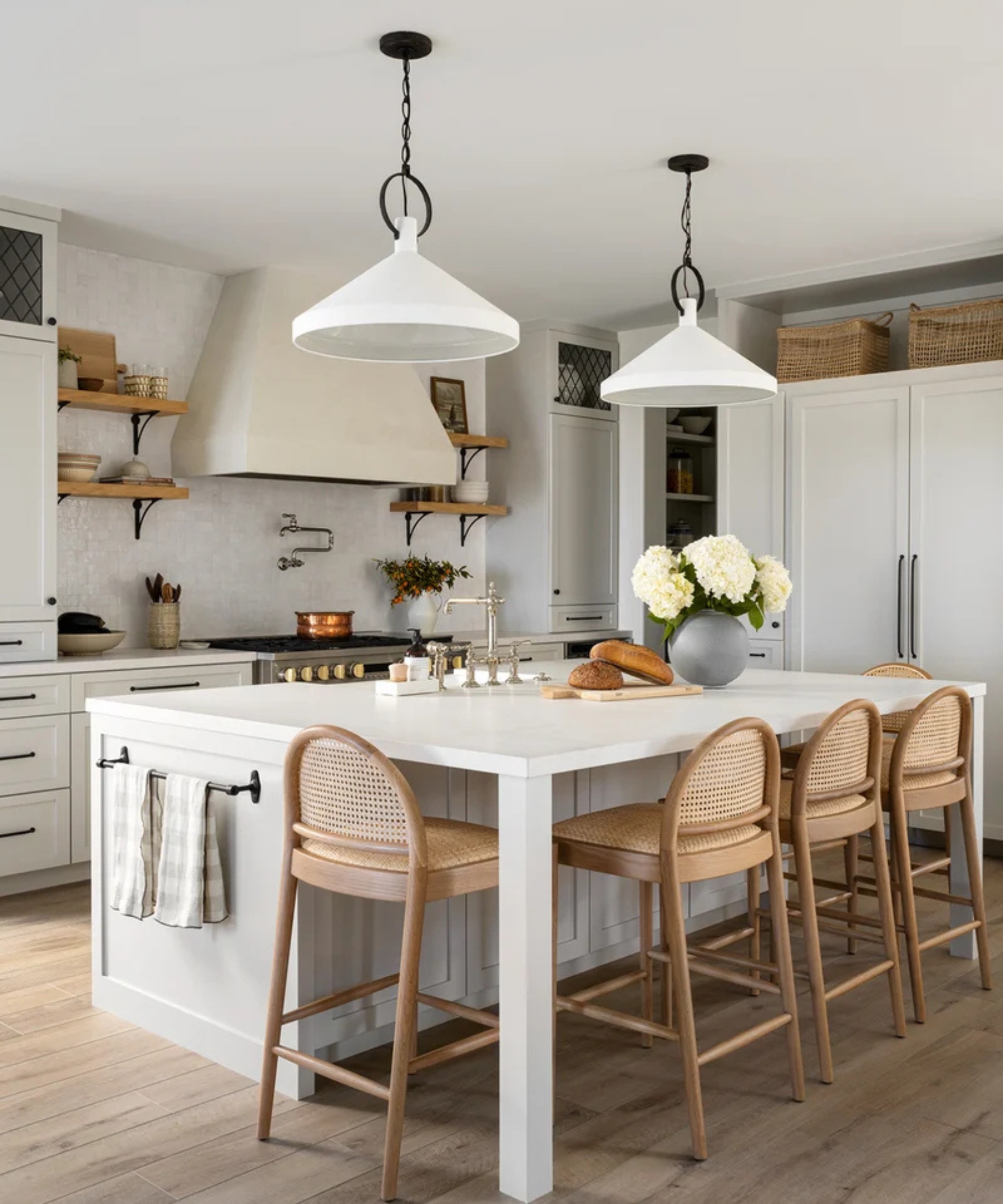 A white kitchen with curbed counter stools around the island and round pendant lights