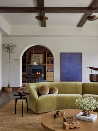 Living room with ochre-green sofa, white walls, jute rug and cobalt blue artwork with round wood coffee table