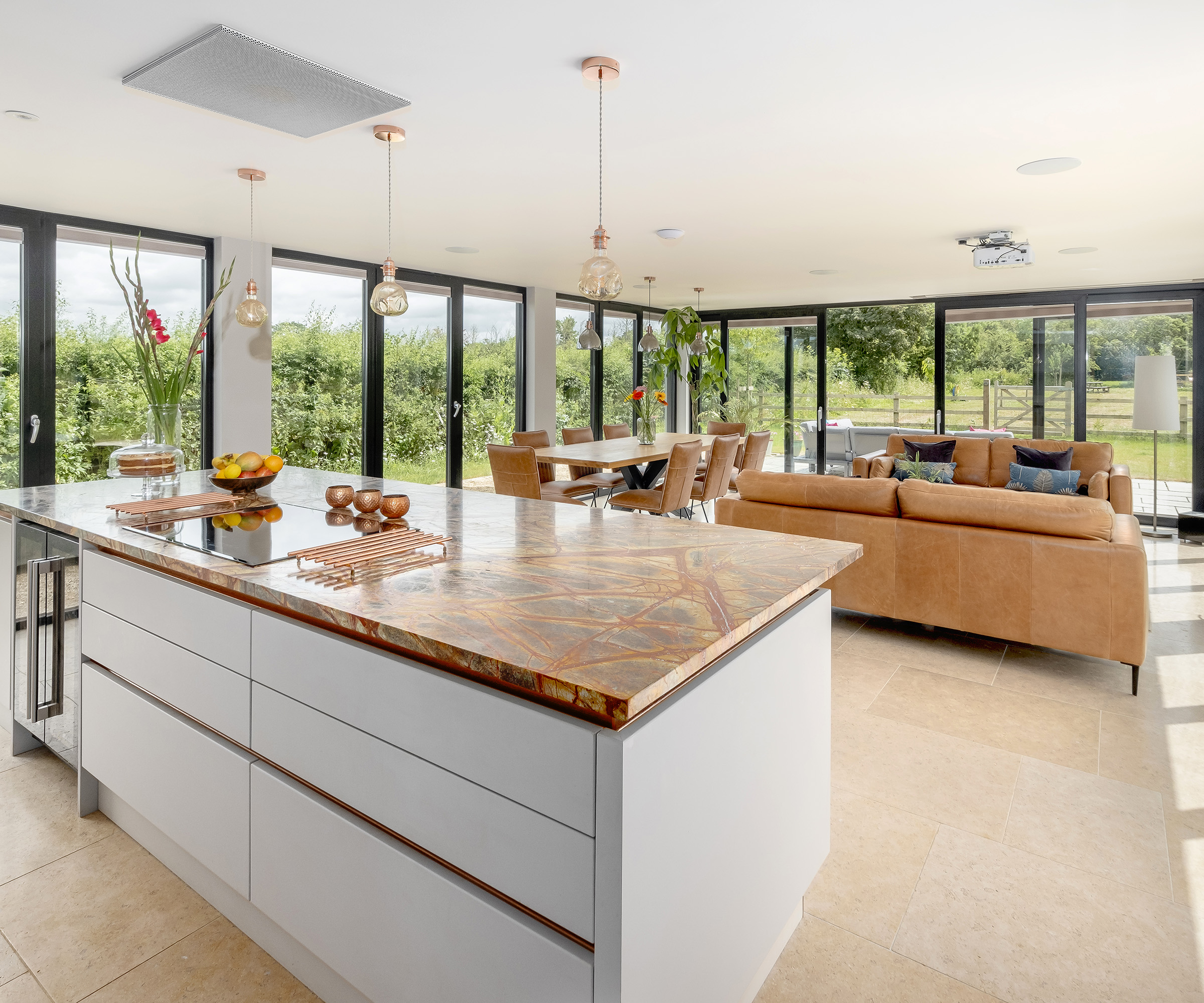 A kitchen diner flooded with natural light from two adjacent walls formed of floor to ceiling glazed doors and window