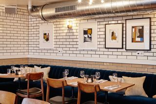 The Hoxton dining room with metro tiles on wall, blue velvet banquette seating and exposed stainless extraction on ceiling