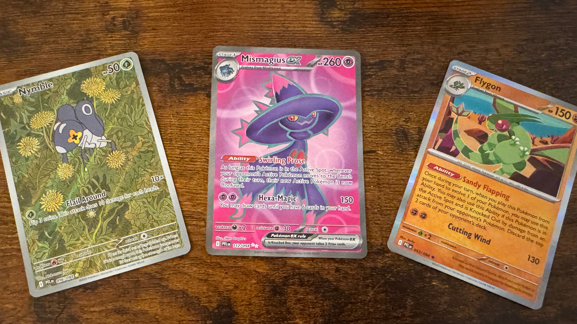 Three Pokemon Phantasmal Flames cards laid out on a wooden surface