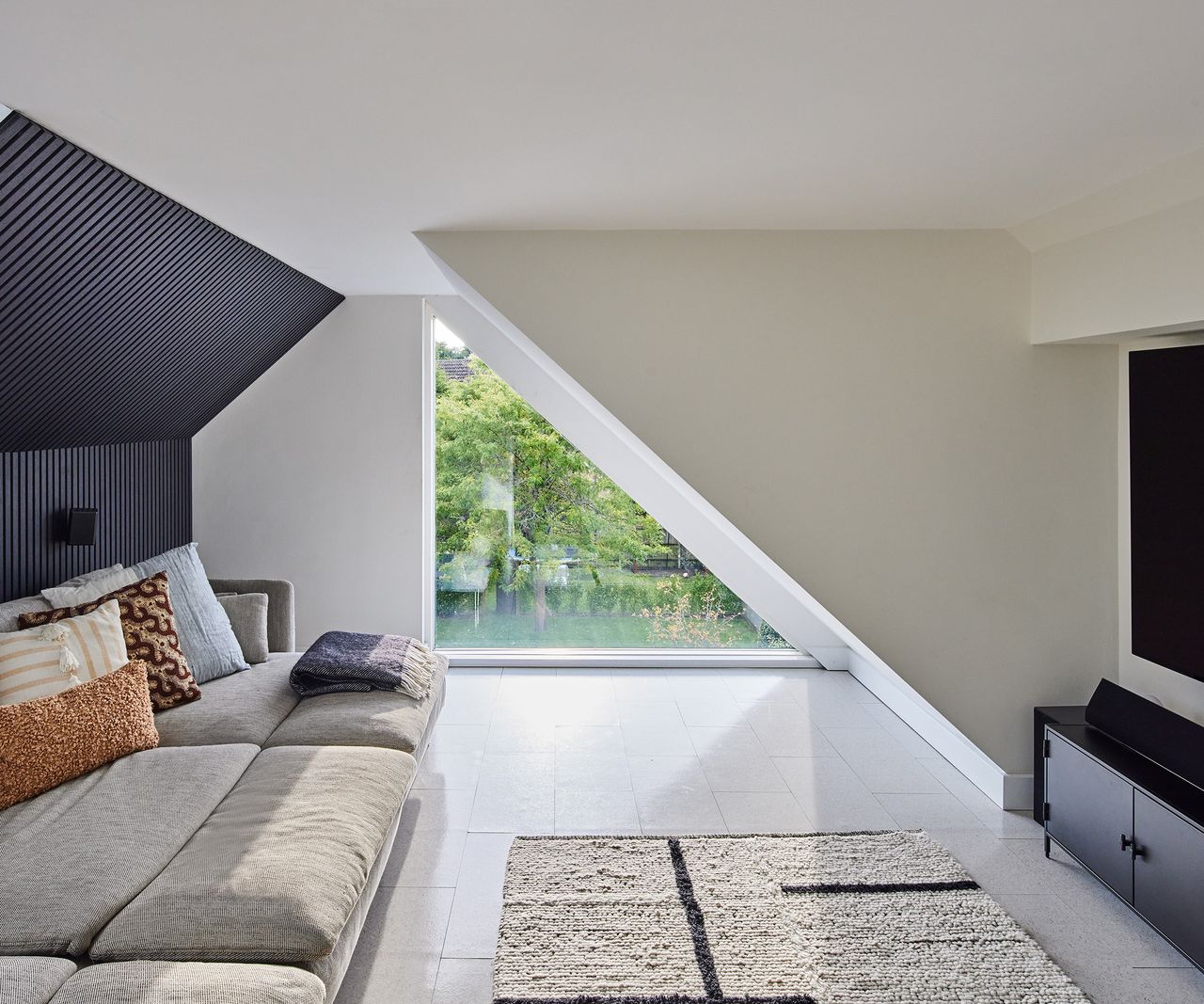 A cosy TV room in the loft of a self build home. The ceiling is low and sloping. There is a wide and comfortable sofa ahd. alarge screen TV