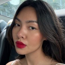 A woman taking a selfie in a car of her makeup look featuring a bold red lip